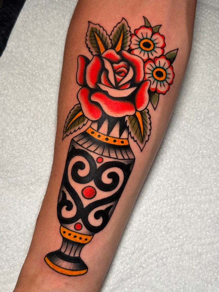 Traditional vase with a red rose tattoo on the forearm